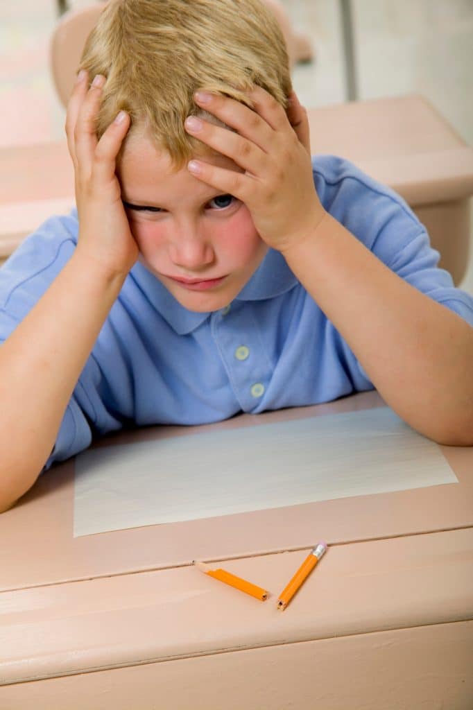 Student with hands on head and broken pencil on desk 